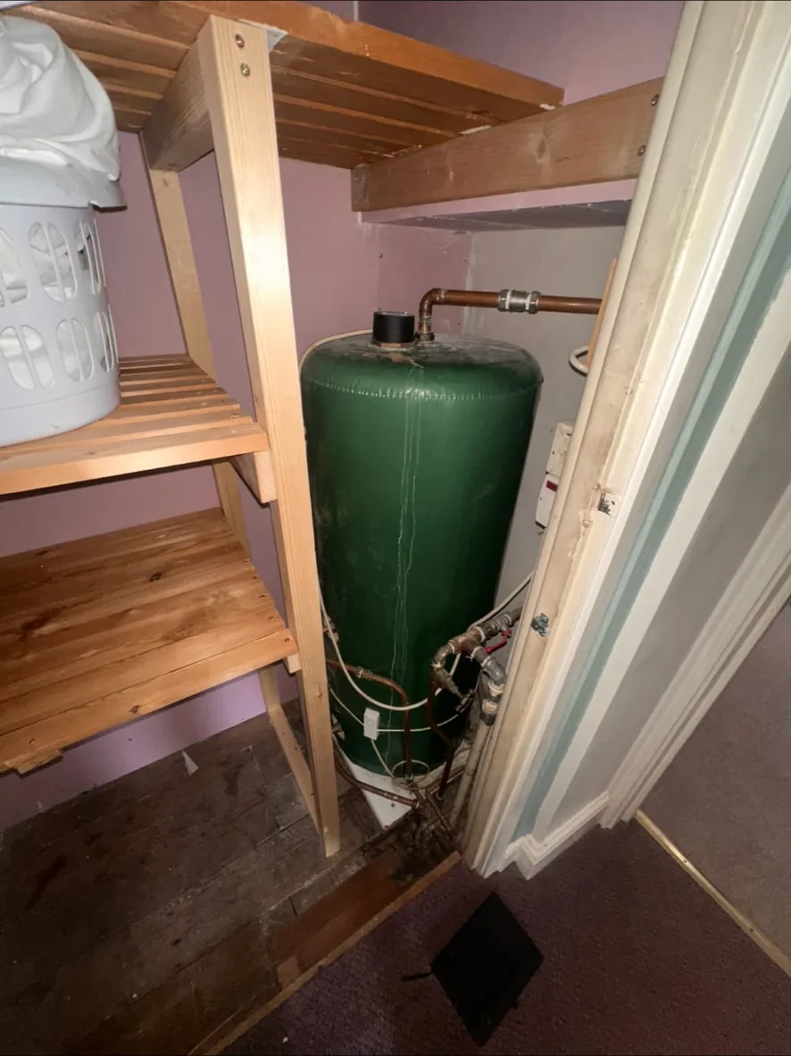 Old green vented hot water cylinder in a cupboard before removal